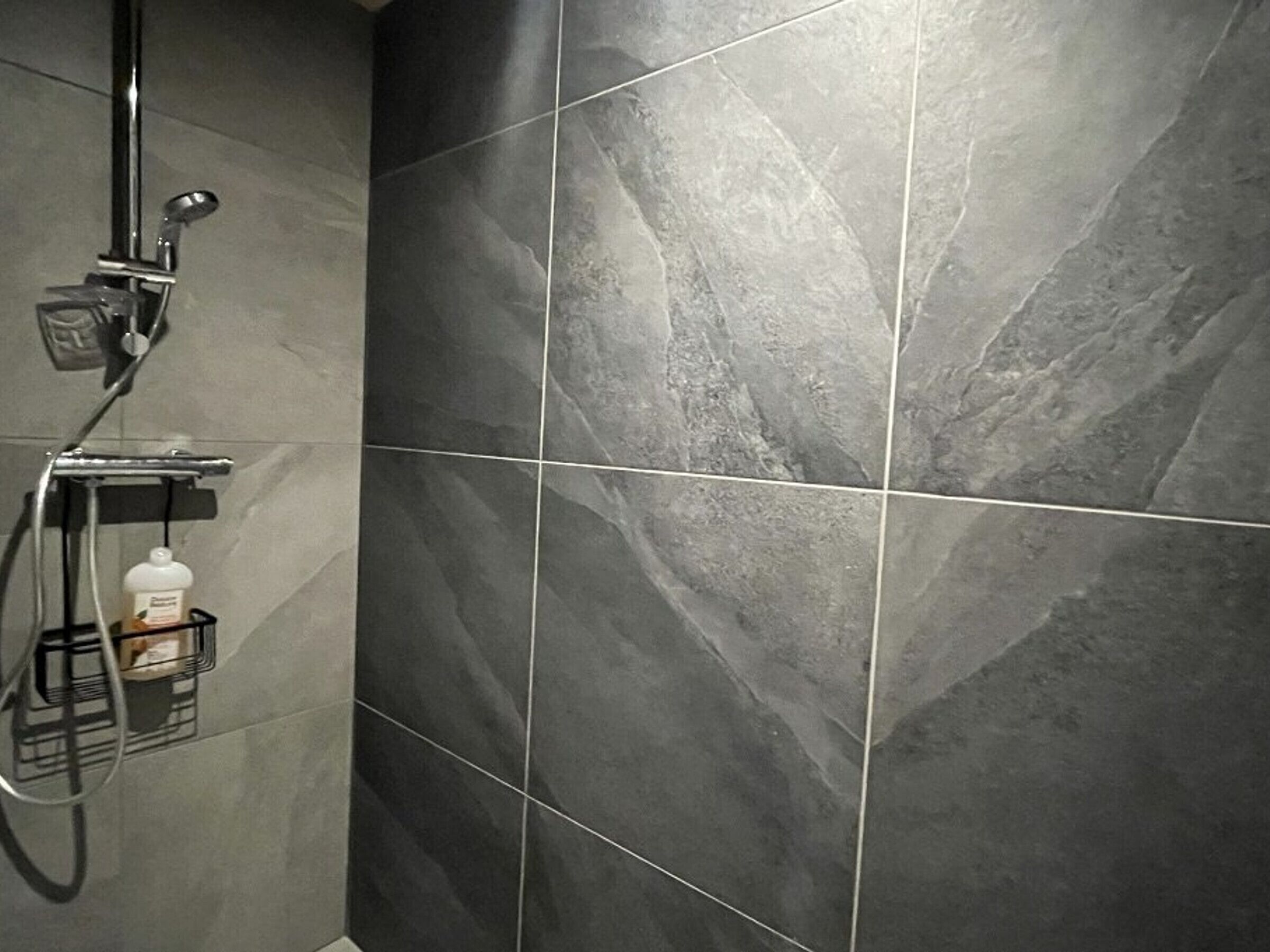A shower area with dark grey tiles and a handheld showerhead.