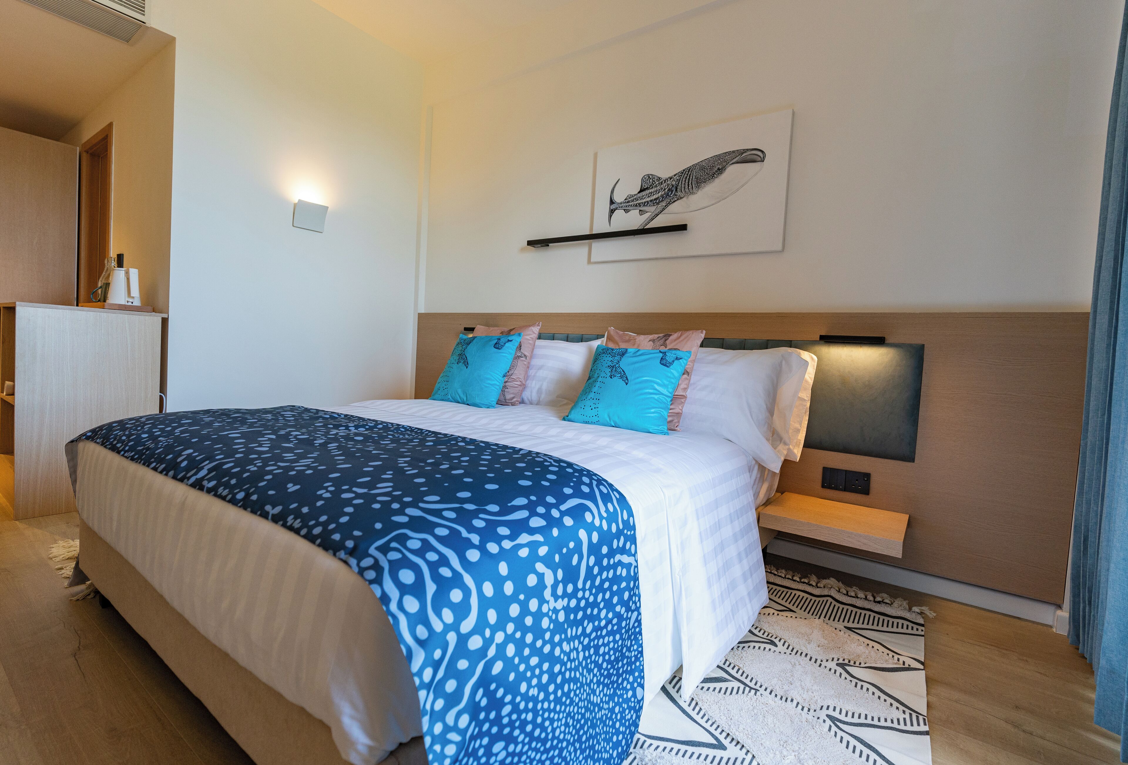 A modern hotel room with a large bed, a bedside table, a wall-mounted TV, and a unique artwork.