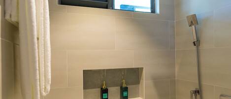 A modern bathroom with a shower, a window, and two bottles of shampoo on a shelf.