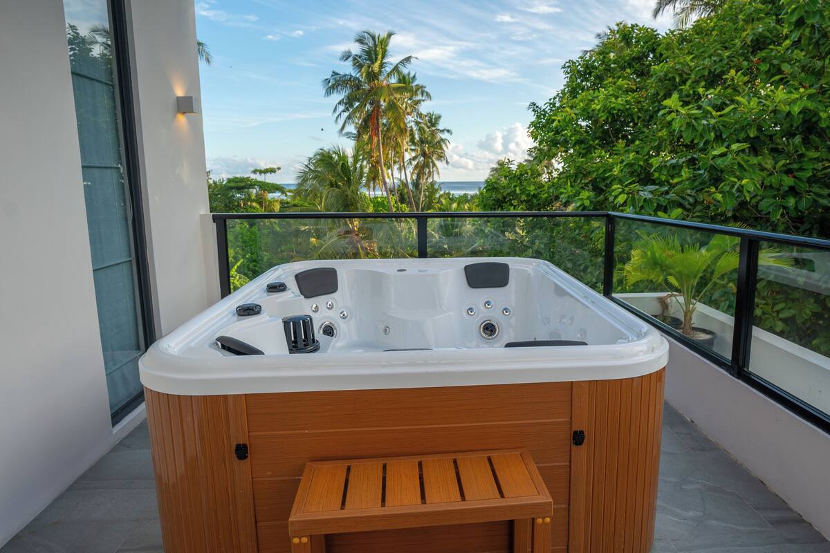 A hot tub on a balcony with a view of the ocean and palm trees.