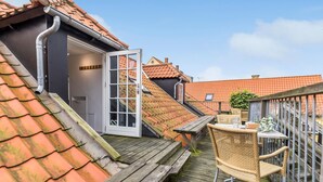 A rooftop terrace with a wooden deck, a wicker chair, and a glass door leading to an upper level.