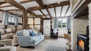 A cozy living room with a fireplace, wooden beams, a sofa, and a chair.