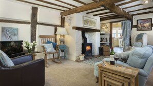 A cozy living room with exposed wooden beams, a fireplace, a sofa, a television, and a table with glasses of wine.