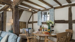 A cozy dining area with a wooden table set for two, surrounded by wooden chairs. A bowl of fruit and a bottle of wine are on the table.