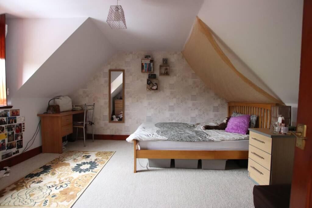 A bedroom with a sloped ceiling, a bed, a dresser, a desk, and a mirror.