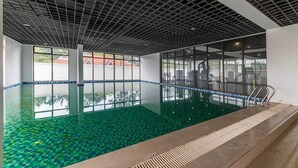 An indoor swimming pool with a tiled floor, a grid-patterned ceiling, and large windows. - Benedictions Homes (Nairobi)