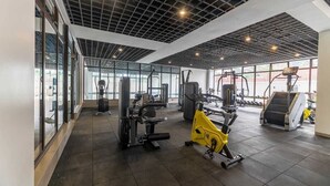 A gym with various exercise equipment, large windows, and a grid-patterned ceiling. - Benedictions Homes (Nairobi)