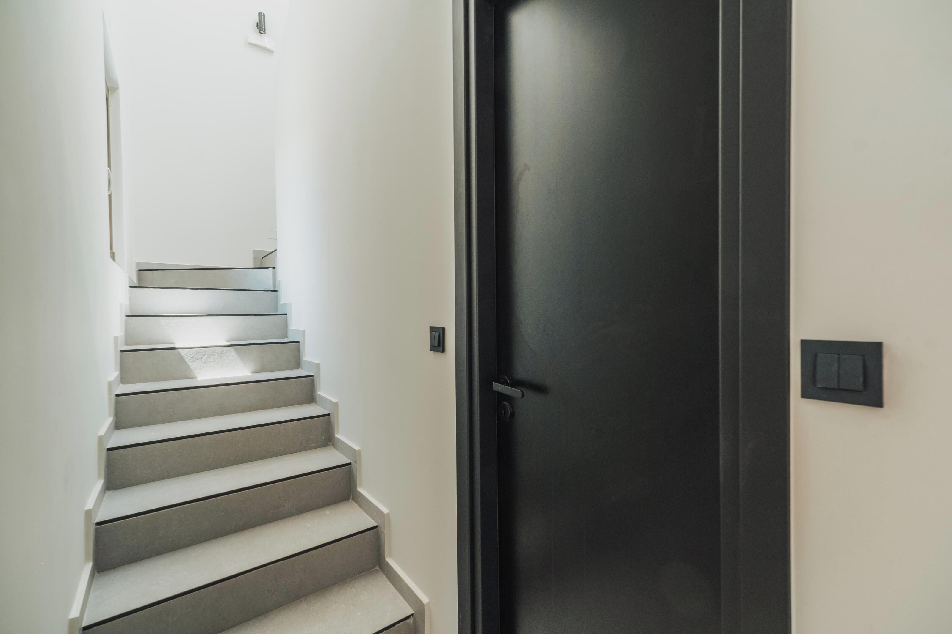 Un escalier menant à une porte sombre, avec un interrupteur sur le mur.