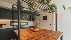 A modern kitchen with a wooden table, hanging plants, and a pineapple in a bowl. - Nos Aqua Villas (Chania)