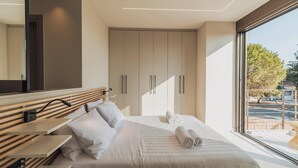 A modern bedroom with a large bed, a bedside table, a TV mounted on the wall, and a wardrobe with sliding doors. - Nos Aqua Villas (Chania)