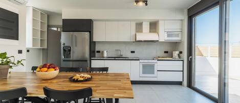 A modern kitchen with white cabinets, a wooden dining table, and a large window.