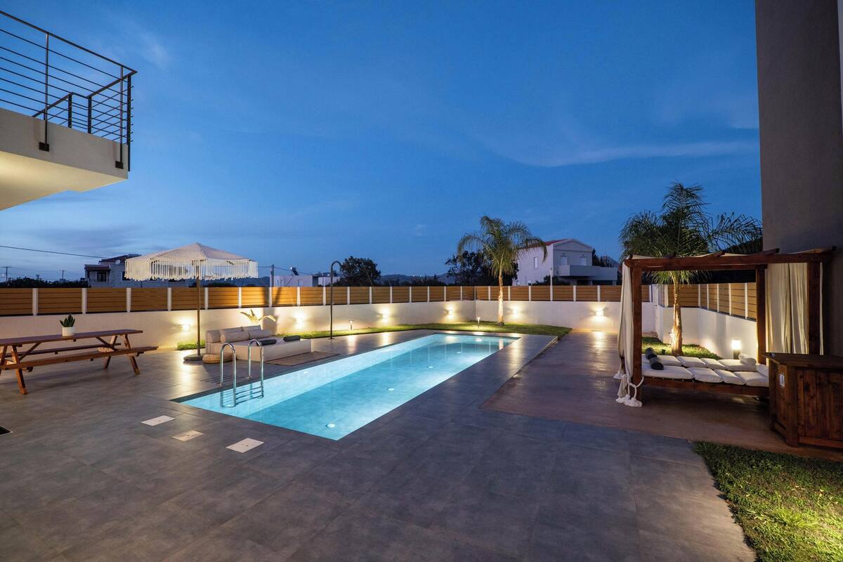 A rectangular swimming pool with a ladder, surrounded by a patio area with a wooden bench and a small table.