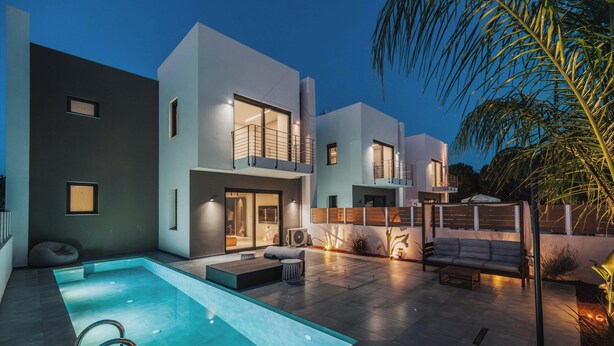A modern residential building with a swimming pool, outdoor seating, and a well-lit patio area. - Nos Aqua Villas (Chania)
