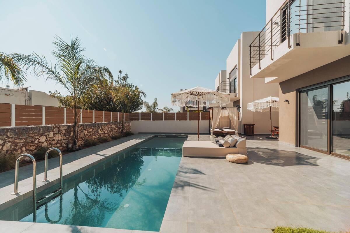A modern outdoor pool area with a stone wall, lounge seating, and a pergola.