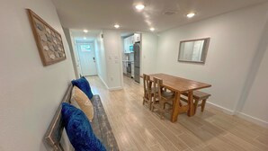 Un vaste espace de vie comprenant un banc en bois, une table à manger avec des chaises, et une cuisine à l’arrière-plan.