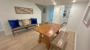 Un coin repas avec une table et des bancs en bois, un banc agrémenté de coussins bleus et une décoration murale représentant des poissons.