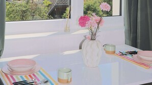 A room with a large window, a vase with flowers, a table with a striped placemat, and a view of a lake and mountains.