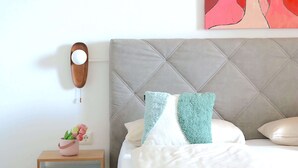 A neatly arranged hotel room with a bed, pillows, a bedside table with a lamp, and a wall-mounted artwork.