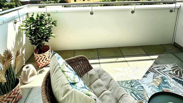 A balcony with a wicker sofa, a potted plant, and a patterned tablecloth.