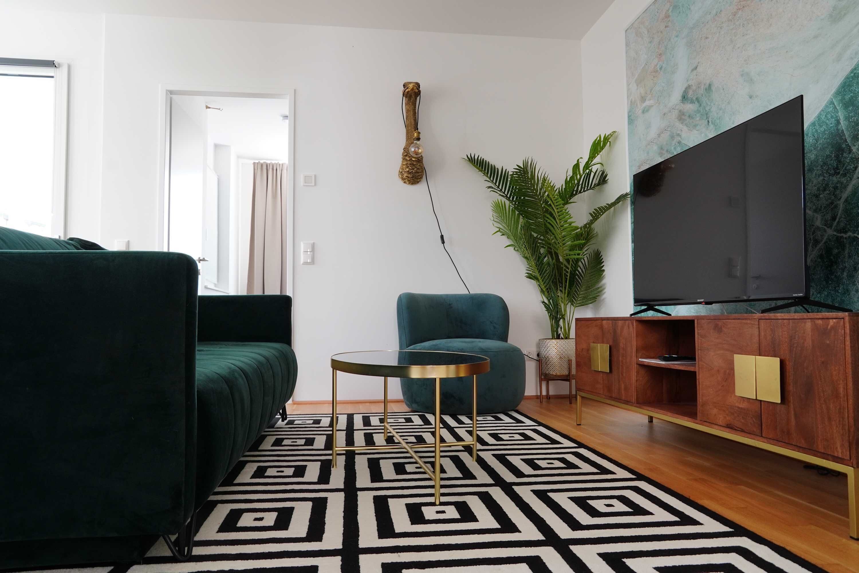 Una sala de estar con sofá, sillón, una mesita redonda, televisor, mueble y planta.