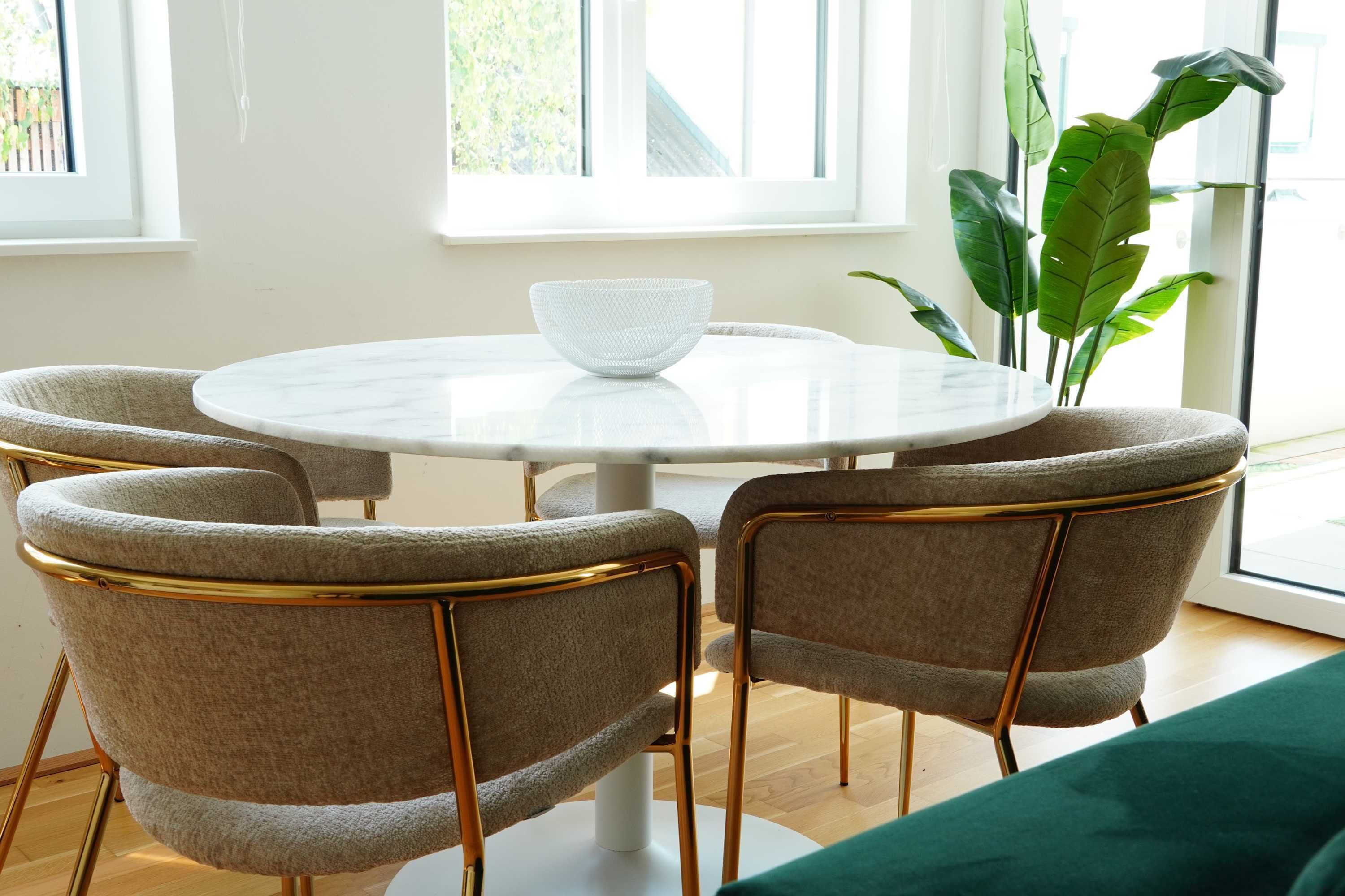 Ein runder Tisch mit einer weißen Schüssel, vier grau gepolsterte Stühle mit goldfarbenen Beinen und ein grünes Sofa.