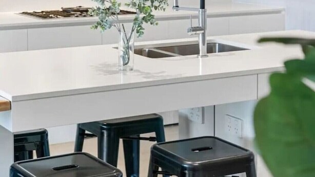 Une cuisine moderne avec un plan de travail blanc, des tabourets noirs et un robinet noir.