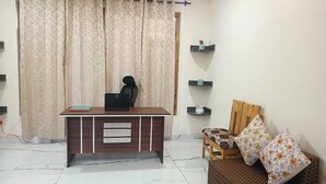 A room with a desk, a chair, a sofa, and a window with curtains. - Heaven Inn Manali (Manali)