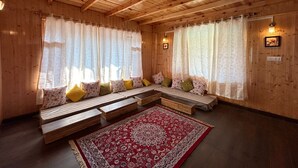 A cozy wooden room with a sofa set, a red patterned rug, and curtains. - Heaven Inn Manali (Manali)