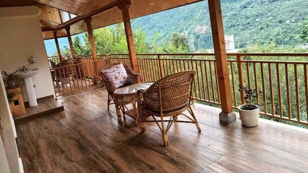 A wooden deck with wicker furniture and a view of a mountainous landscape. - Heaven Inn Manali (Manali)