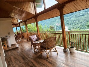 Una terraza de madera con mobiliario de mimbre y vistas a un paisaje montañoso.
