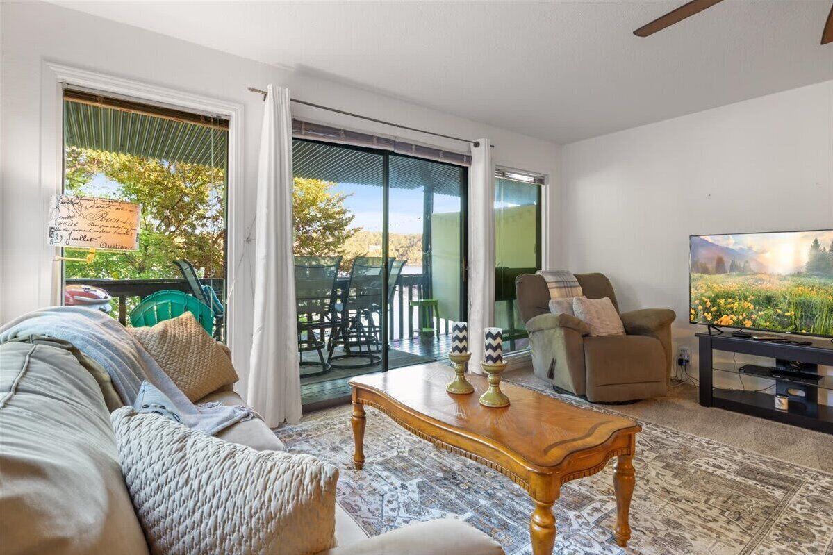 A living room with a sofa, a coffee table, a TV, and a sliding glass door leading to an outdoor area with chairs and a table.