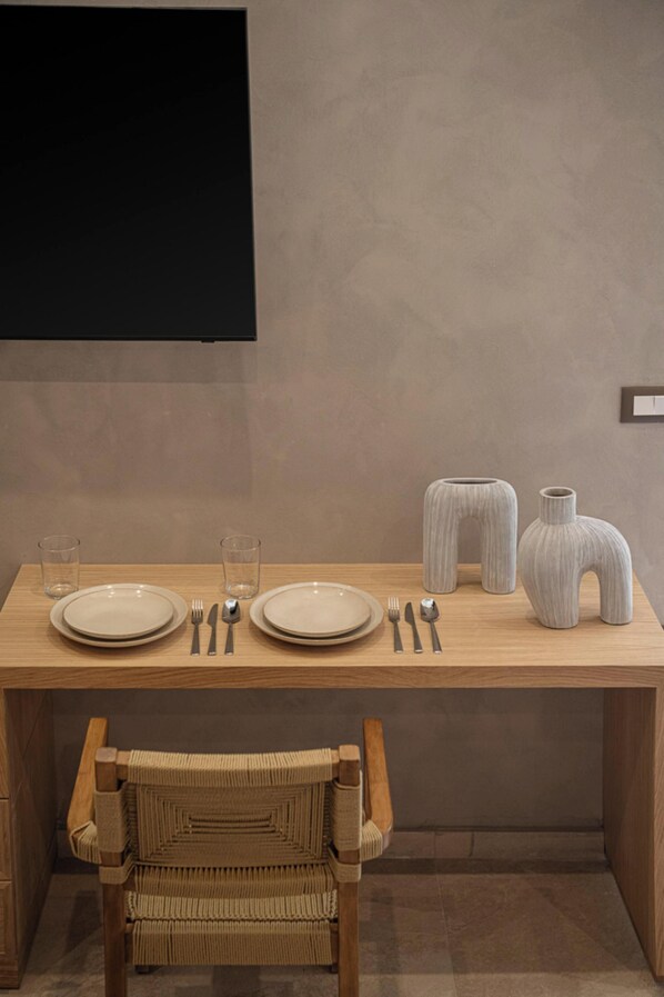 Una mesa de comedor dispuesta con platos, cubiertos y vasos, junto con dos jarrones decorativos y una silla de mimbre.