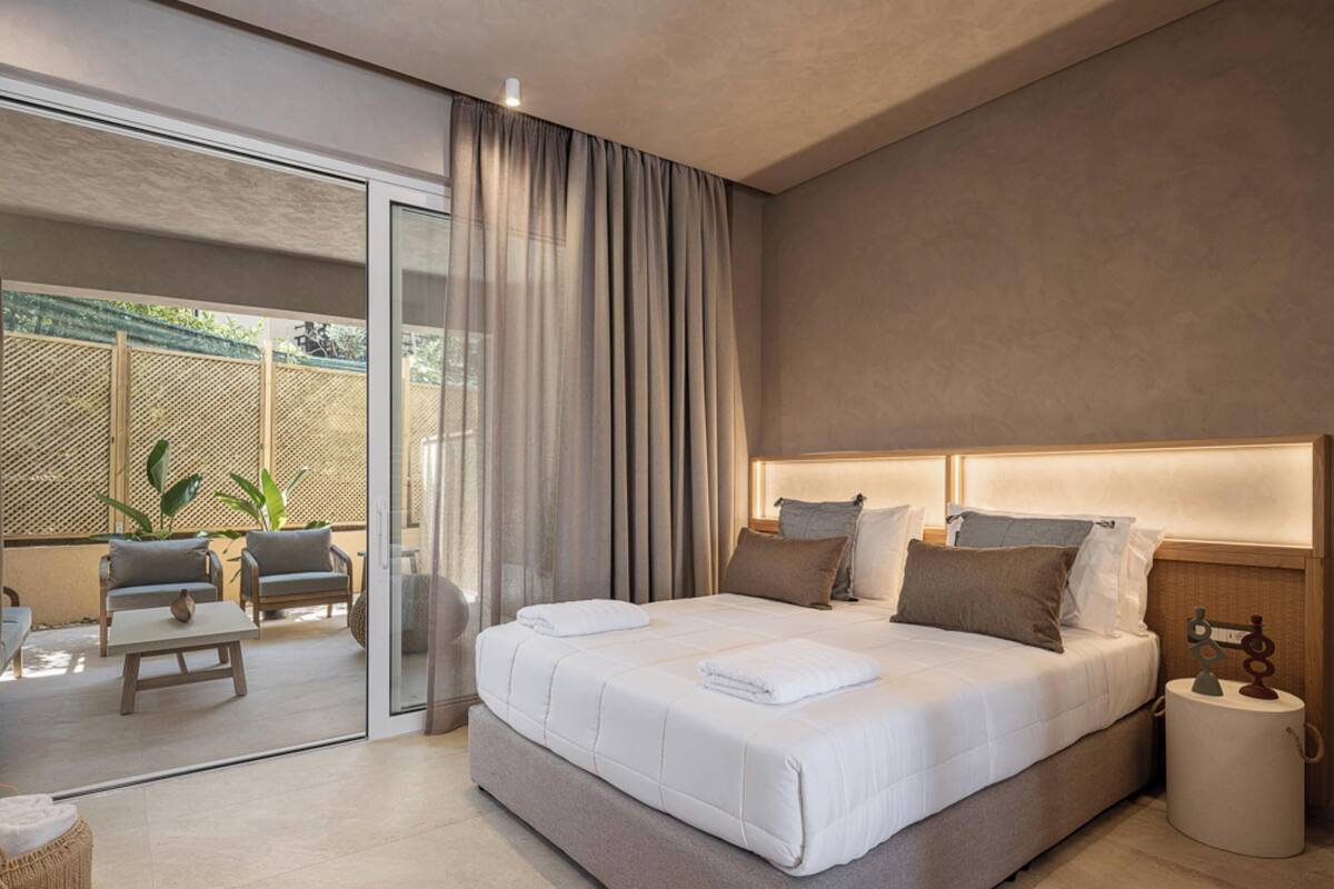 Une chambre moderne dotée d’un grand lit, d’une porte vitrée donnant sur un balcon et d’un petit coin salon avec une table et des chaises.