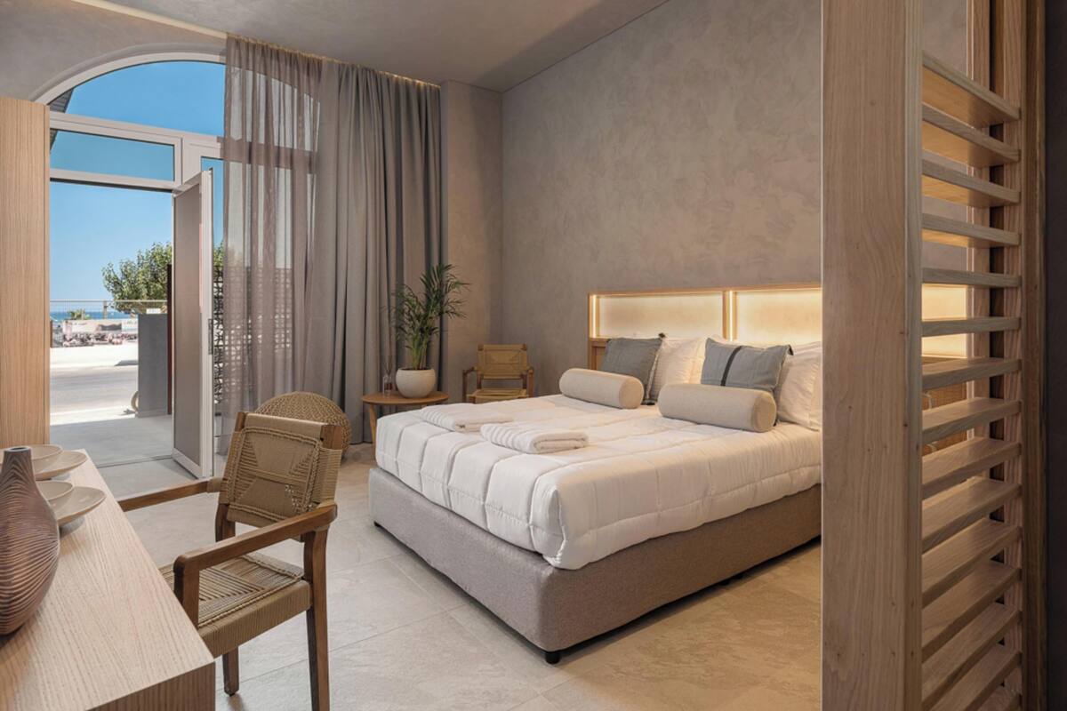Une chambre moderne avec un grand lit, une tête de lit en bois, une petite table avec une plante et une vue sur l’extérieur.