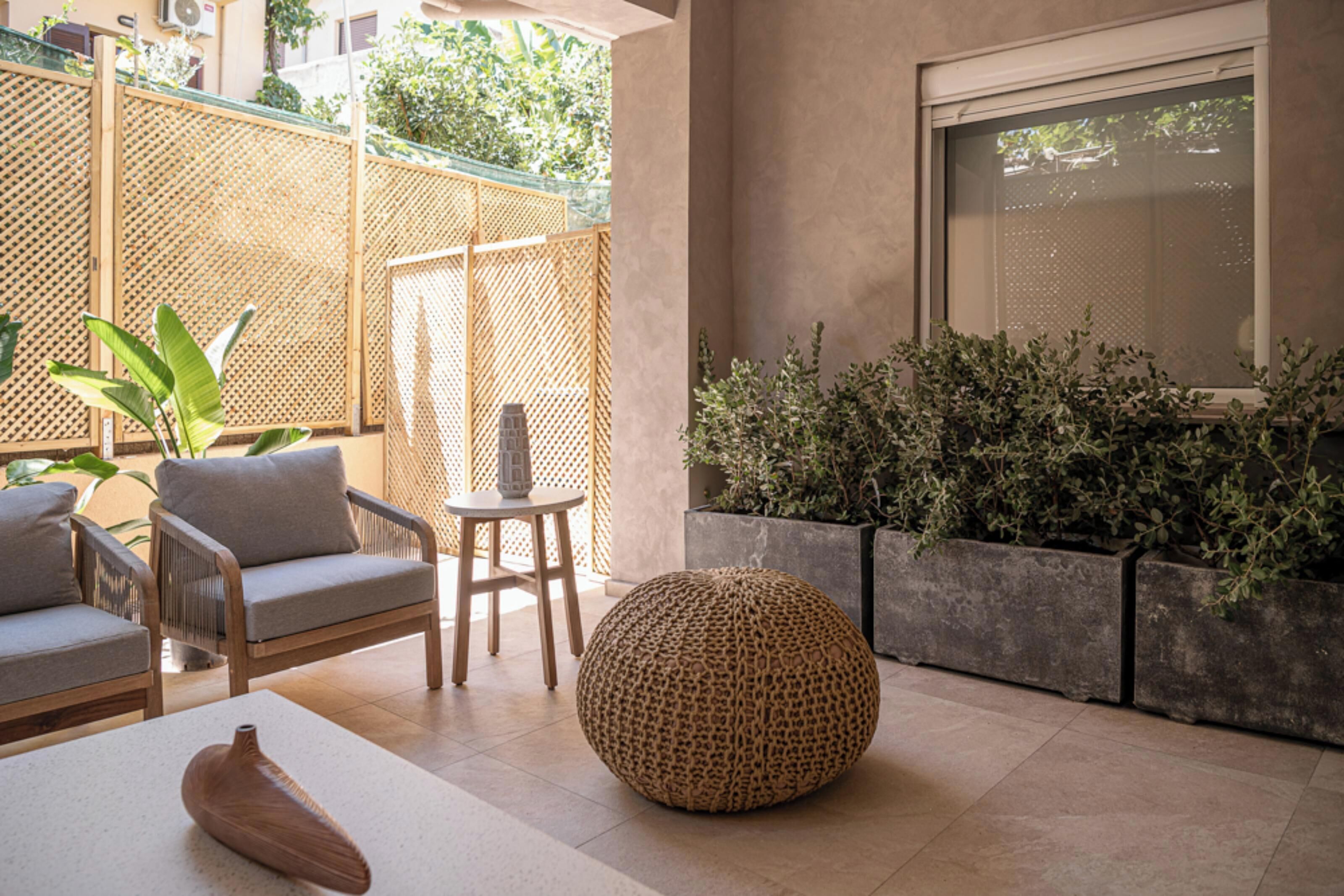 A modern outdoor seating area with a sofa, chairs, a round pouf, and potted plants.