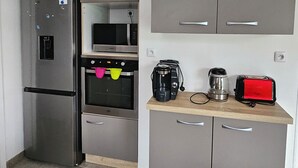 Ett kompakt kök med ett kylskåp, en ugn, en mikrovågsugn och en kaffebryggare i rostfritt stål, placerade på bänkskivan.