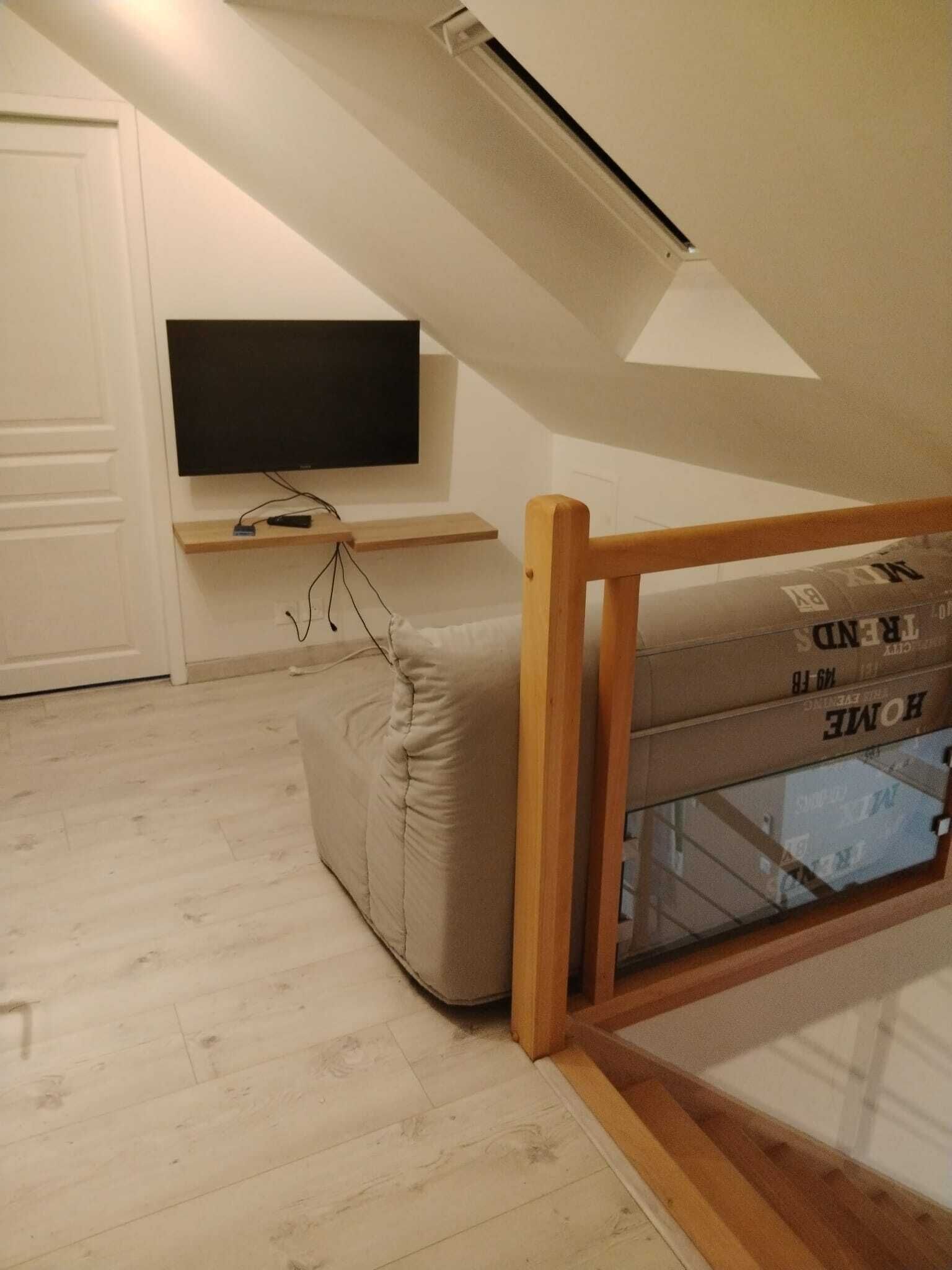 A room with a loft bed, a mounted TV, and a wooden shelf.