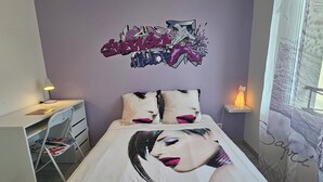 Ett sovrum med en säng, ett skrivbord, en stol, en lampa och en vägg med graffiti.