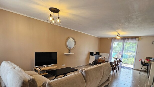 Ett vardagsrum med en stor beige soffa, en platt-TV och en matplats med ett bord och stolar.