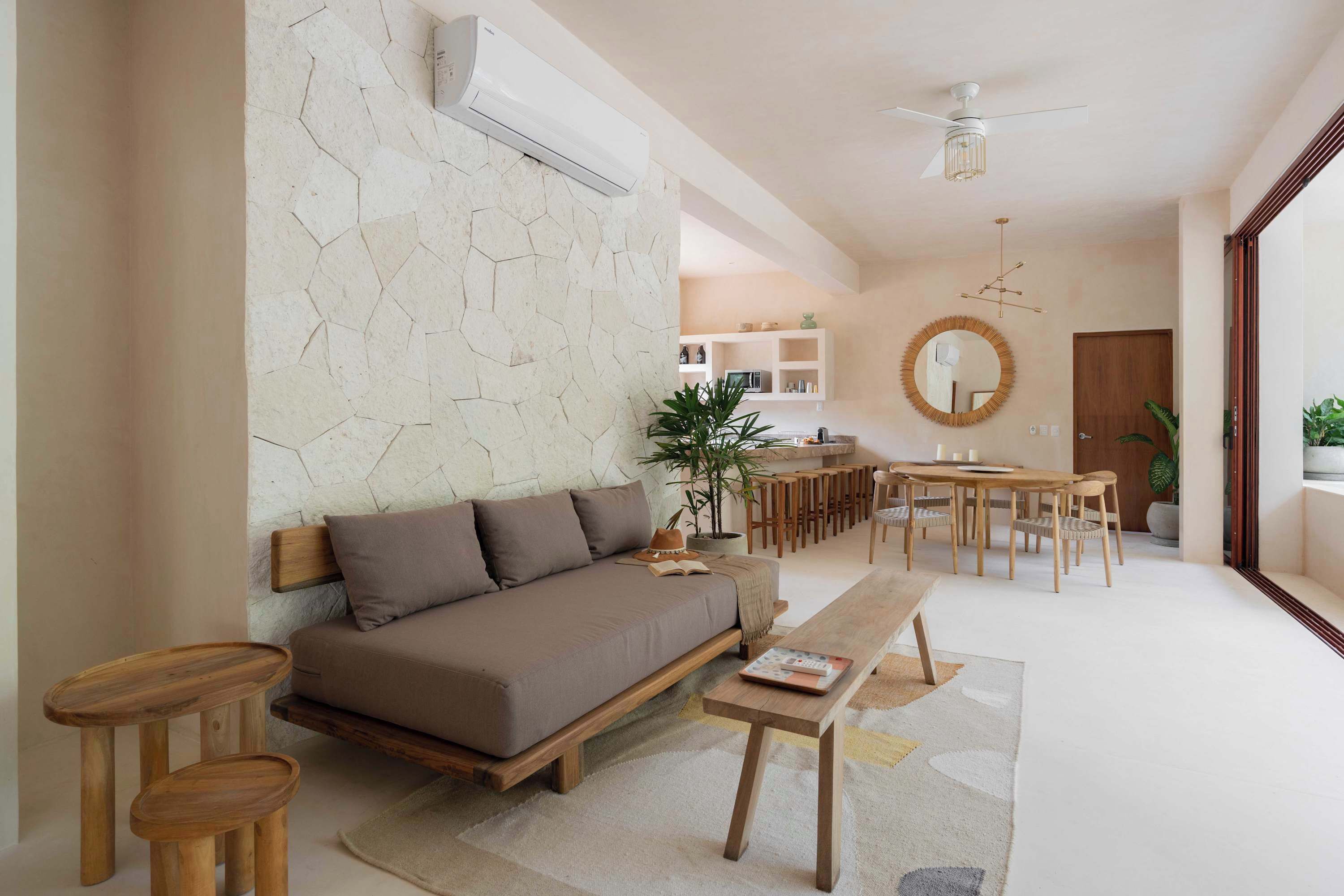 A modern living room with a sofa, wooden side tables, a dining area with a round table, and a kitchen in the background.