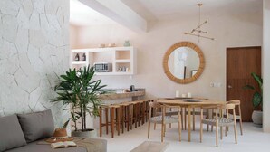 A modern living room with a sofa, a dining table with chairs, a large mirror, and a kitchen area with shelves and appliances. - Catch Soulful Vibes at AHAL II! Enjoy a private plunge pool and a communal pool! (Tulum)