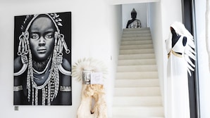 A modern interior with a large black and white portrait, a staircase leading to a Buddha statue, and a white statue with a feathered headpiece. - My Rental Homes - Villa Seahorse private pool and air conditioning (Cala Llonga)