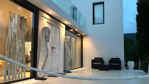 A modern building with large glass doors, a rope barrier, and outdoor seating. - My Rental Homes - Villa Seahorse private pool and air conditioning (Cala Llonga)