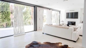 A modern living room with a white sofa, a large wooden coffee table, and a flat-screen TV mounted on the wall. - My Rental Homes - Villa Seahorse private pool and air conditioning (Cala Llonga)