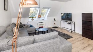 A modern living room with a large sofa, a floor lamp, a TV, and a small table. - 4 Person Holiday Home in Frederikshavn (Frederikshavn)