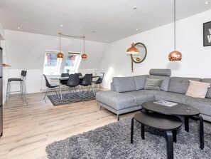 A modern living room with a grey sectional sofa, a round coffee table, and a dining area with a table and chairs.