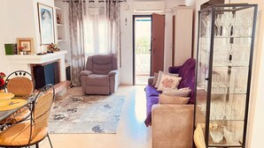 Een woonkamer met een open haard, een bank, een eettafel met stoelen, en een glazen kast met wijnglazen.