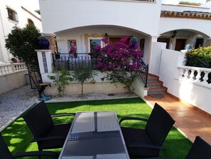 A patio with a table and chairs, surrounded by a garden with artificial grass and a variety of plants.