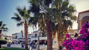 Een terras met buitenmeubilair, palmbomen en bougainvilleablaadjes.