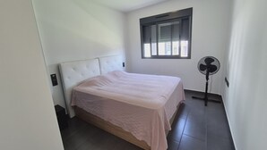 Ein Schlafzimmer mit einem Bett, einem Standventilator und einem Fenster.